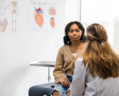 An image of a women sitting on an examination bed listening to a female doctor sitting opposite her