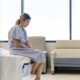 Woman sat on hospital bed in a gown looking sad